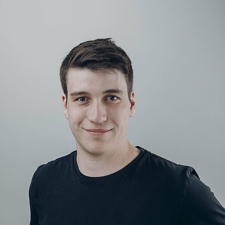 Tobias Brey schmunzelnd mit dunkelblauen T-Shirt vor hellem Hintergrund.