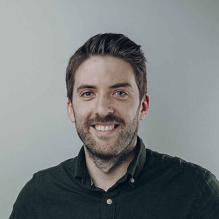Andreas Mangold lächelnd mit dunkelgrünen Hemd vor hellem Hintergrund