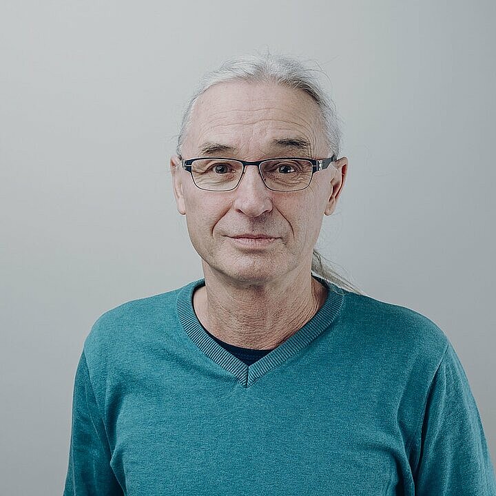 Christian Heim schmunzelnd mit Brille und mit hellblauen Pullovervor hellem Hintergrund