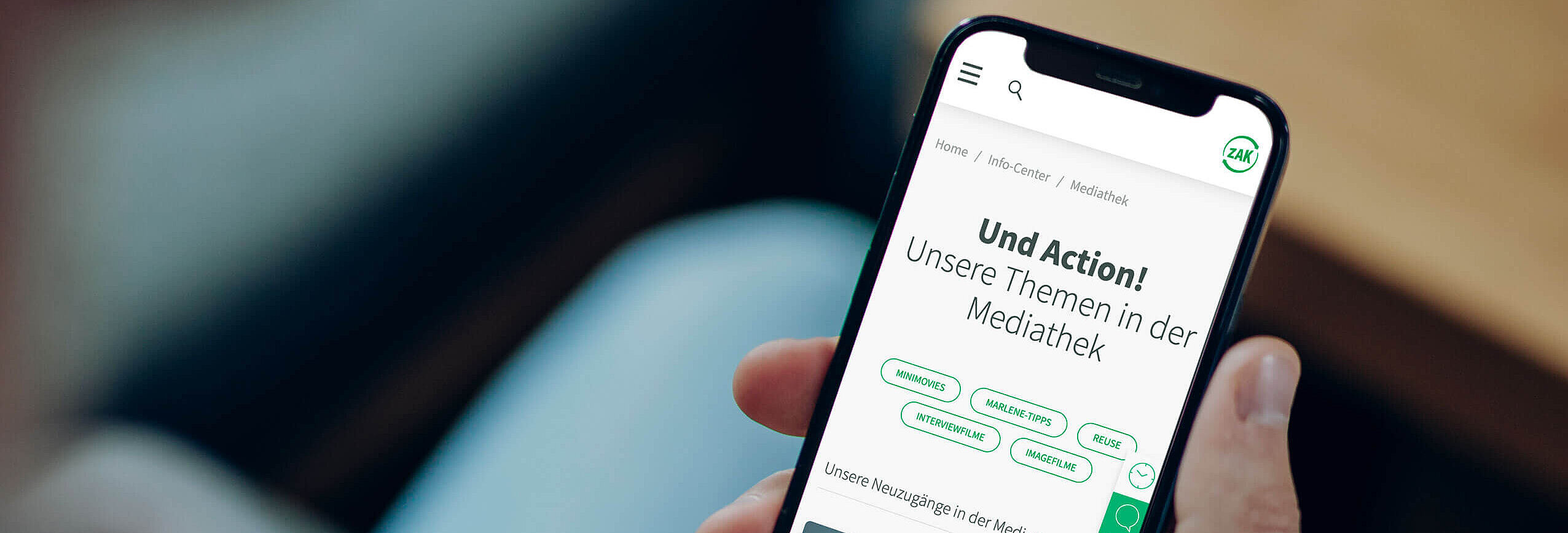 Person hält Smartphone mit geöffneter Mediathek-Seite von ZAK, Überschrift 'Und Action! Unsere Themen in der Mediathek' sichtbar