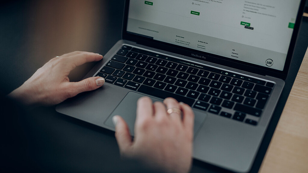 Person sitzt am Laptop und scrollt durch die ZAK-Website