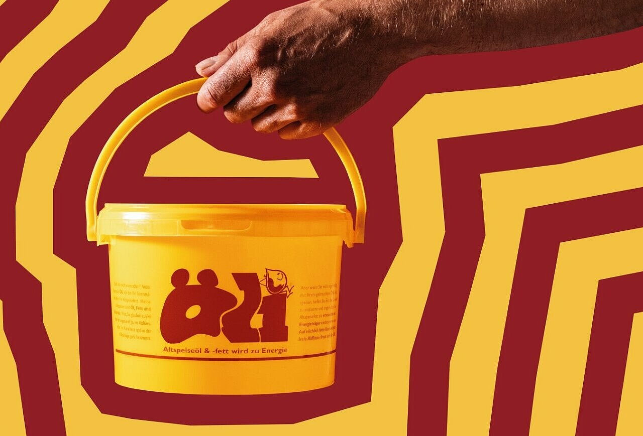 Gelber Eimer mit Aufschrift "Öli" wird von einer Hand vor einem rot-gelben Hintergrund gehalten.
